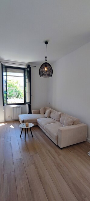 Ein modernes Wohnzimmer mit großem Fenster, einer Couch, einem kleinen runden Tisch und einer Pendelleuchte.