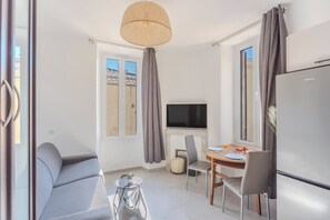 Ein modernes Zimmer mit einer Couch, einem Esstisch mit Stühlen, einem Fernseher und einem Kühlschrank.