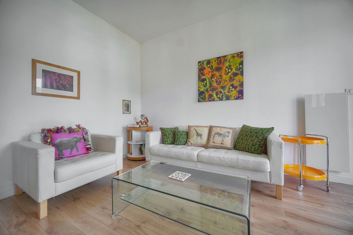 A modern living room with a white sofa, a glass coffee table, and a colorful abstract painting on the wall.