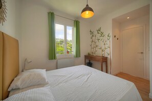 A bedroom with a bed, a bedside table with a lamp, a window with curtains, and a door. - 12251546 FRGK Isola Bella ` 2-room, high-speed Wi-Fi, air conditioning ` (Cannes)