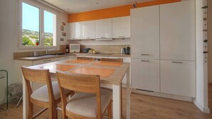 A modern kitchen with white cabinets, a dining table with chairs, and a view through large windows. - FRGK Isola Bella Comfortable apartment (Cannes)