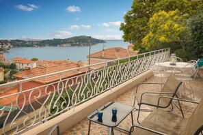 A balcony with a view of a body of water and a distant hill. - Question: "Breathtaking Ocean Views in Villefranche" (Villefranche-sur-Mer)