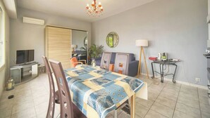 Ein Wohnzimmer mit Fernseher, einem Esstisch, einer Chandelier, einem Spiegel und einer Couch.