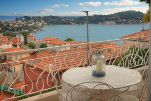 A balcony with a table and a bottle, overlooking a coastal town with terracotta roofs and a body of water. - Question: "Breathtaking Ocean Views in Villefranche" (Villefranche-sur-Mer)