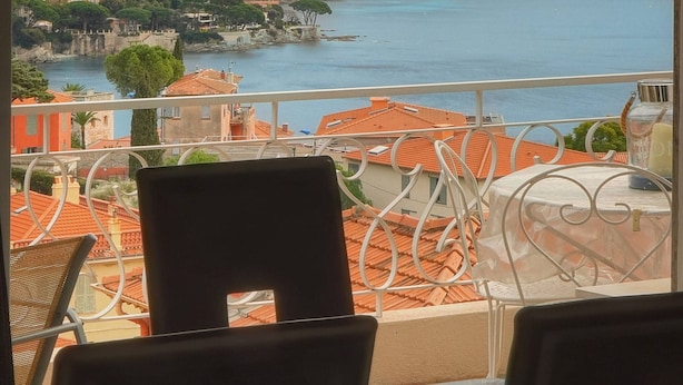 Ein Balkon mit Stühlen und Tisch, mit Blick auf eine Küstenstadt, Gebäude und ein Gewässer.