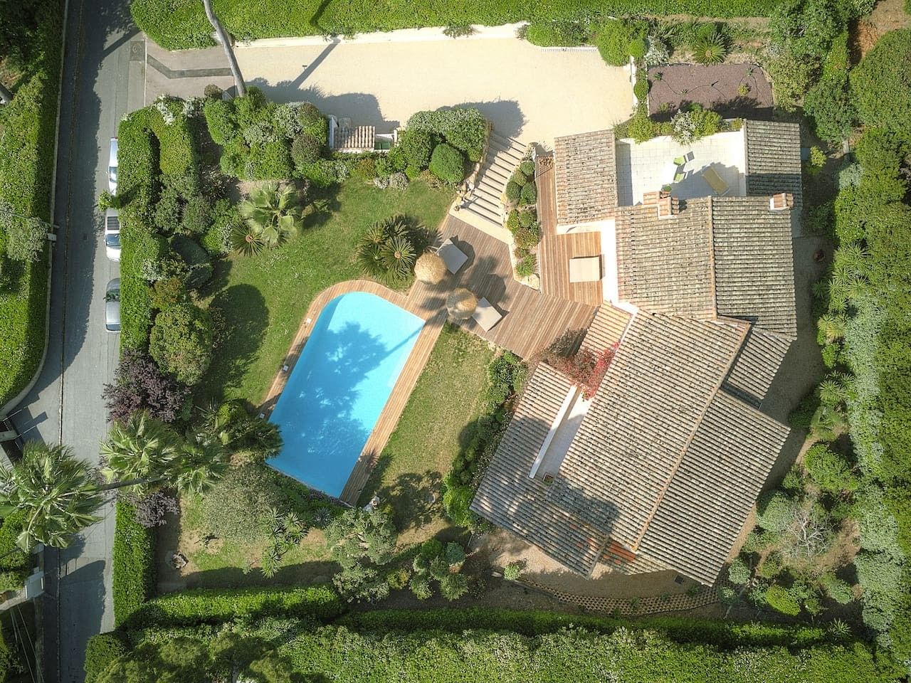 Oversigtsbillede af en bolig med swimmingpool, træterrasse og belagt indkørsel.