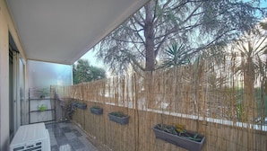 Un balcone riparato con recinto in bambù, piante in vaso e un grande albero sullo sfondo.
