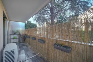 A covered balcony with a bamboo fence, potted plants, and a large tree in the background. - FRGK Tamaris Apartment Antibes Terrace, AC & Ultra (Antibes)