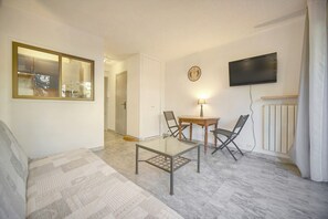 A living room with a glass table, two chairs, a sofa, a TV mounted on the wall, and a clock. - 13107732 Frgk Tamaris Antibes Terrace: Air Conditioning & Ultra-Fast Wi-Fi (Antibes)