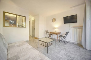 A living room with a glass-top coffee table, two chairs, a small wooden table with a lamp, a flat-screen TV, and a large mirror. - FRGK Tamaris Apartment Antibes Terrace, AC & Ultra (Antibes)