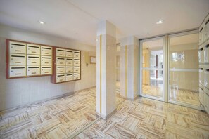 A hallway with a patterned floor, a wall-mounted mail slot system, and a glass door leading to another room. - FRGK Tamaris Apartment Antibes Terrace, AC & Ultra (Antibes)