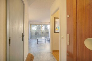 Ein Flur, der zu einem Raum mit einer Schiebetür, einem kleinen Tisch und einer Holztür mit Lichtschalter führt.