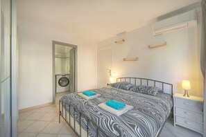Ein Schlafzimmer mit einem Bett, Nachttischen, einem Spiegel, einer Waschmaschine und einer Wandklimaanlage.