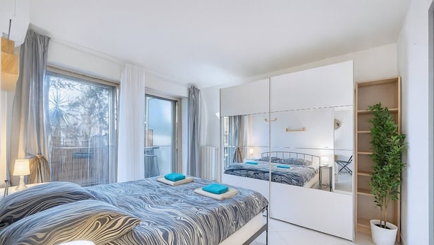 Una camera da letto moderna con un letto grande, un armadio, una pianta in vaso e una finestra con tende.