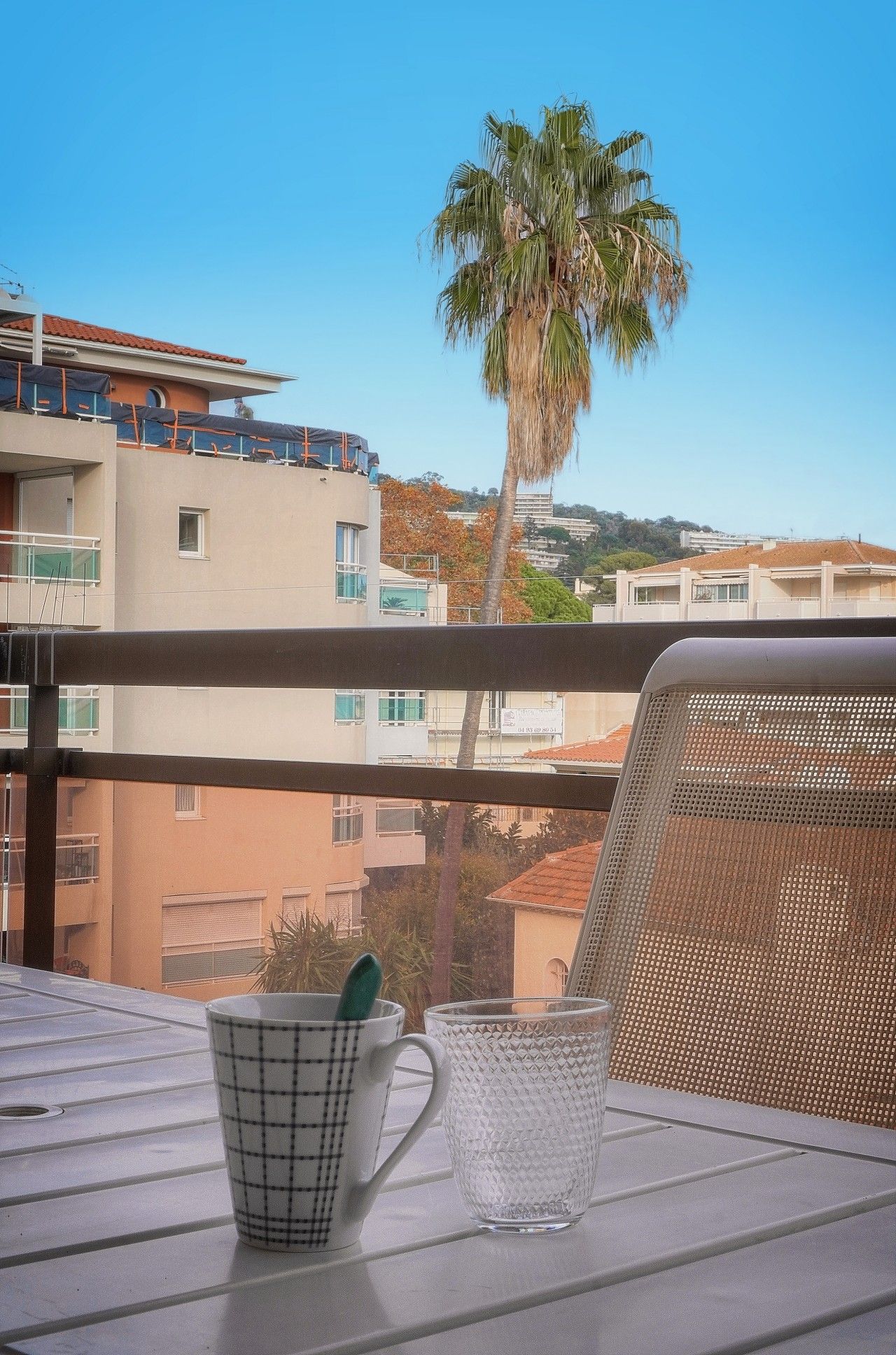A balcony with a table, two cups, and a chair.