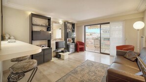 A modern living room with a sofa, a red chair, a TV, a bar area, and a balcony with a view. - ATHENA (Cannes)