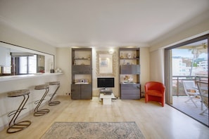 Ein modernes Wohnzimmer mit Fernseher, Barhocker, einem roten Sessel und einem Balkon mit Blick.