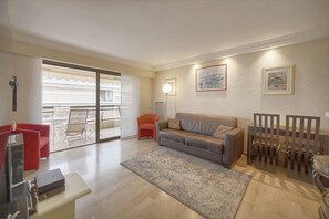 Ein Wohnzimmer mit einer Couch, einem roten Sessel, einem Glastisch und einem Essbereich mit Stühlen.