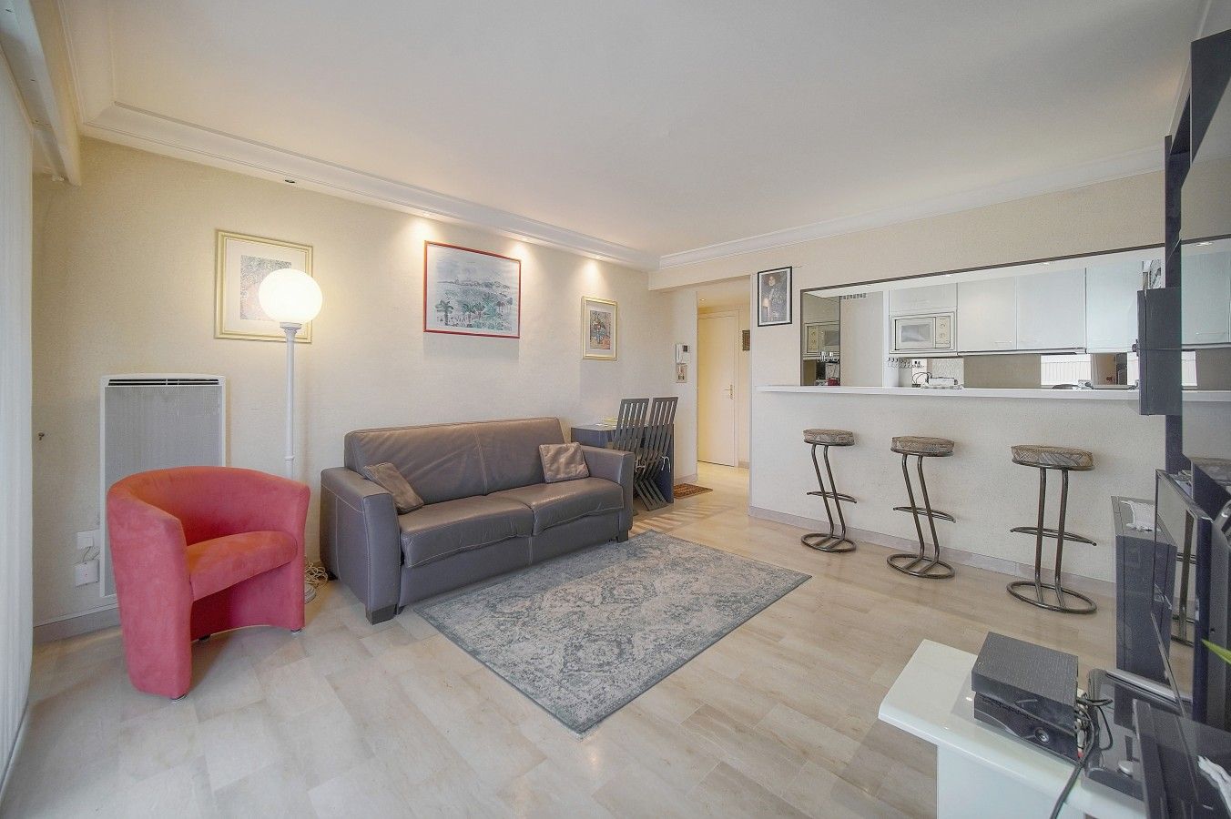 Una sala de estar moderna con un sofá gris, una silla roja y una zona de cocina con taburetes de bar.