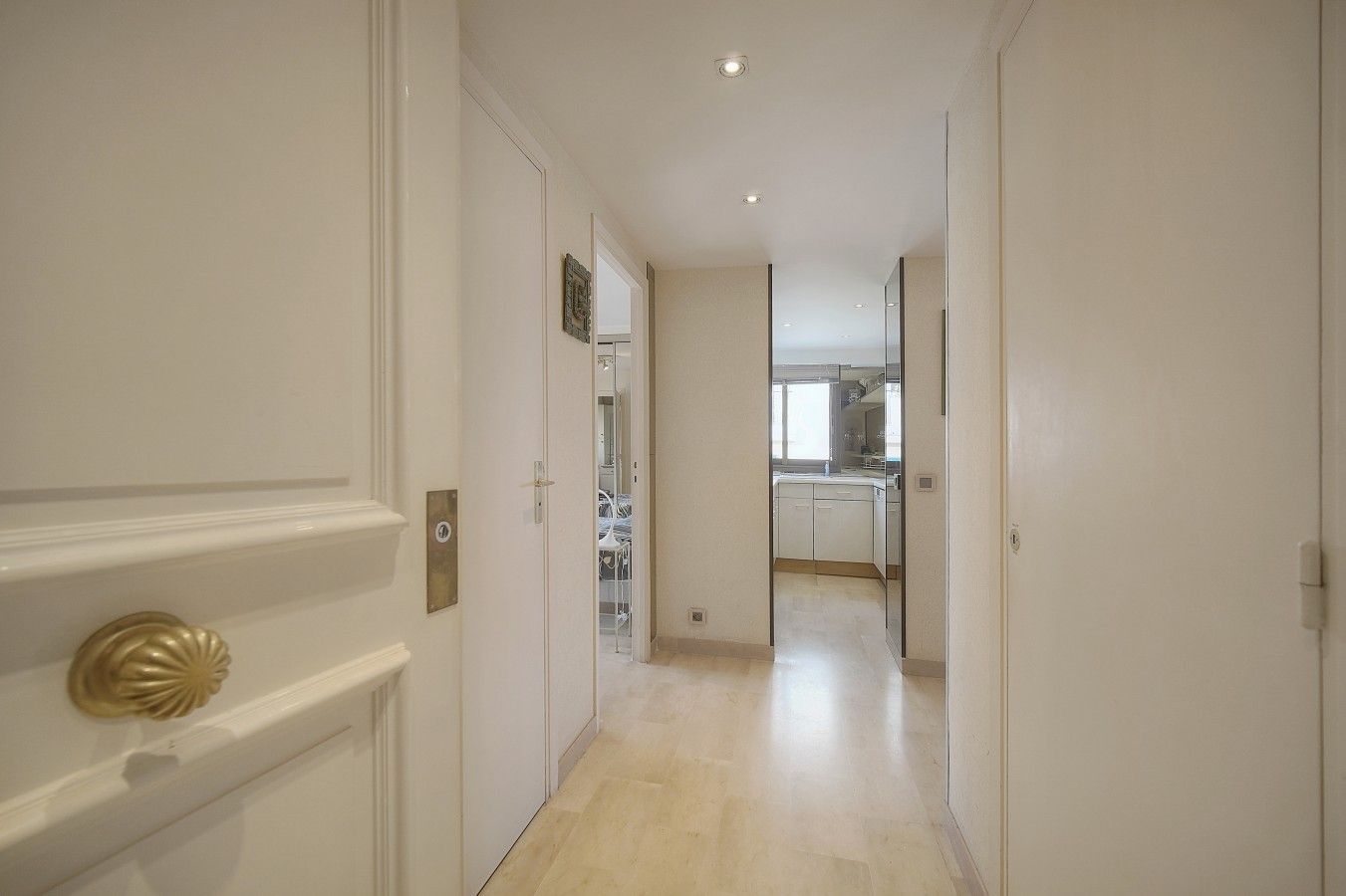 A hallway leading to a kitchen with white cabinetry and a light-colored floor.