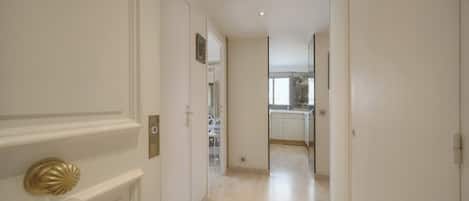 A hallway leading to a kitchen with white cabinetry and a light-colored floor.