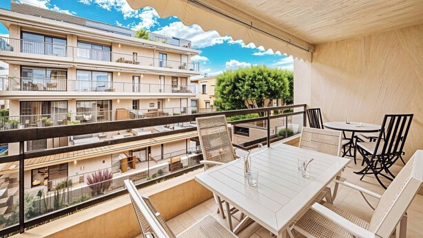 A balcony with a table and chairs, overlooking a multi-story building with balconies and a tree. - ATHENA (Cannes)