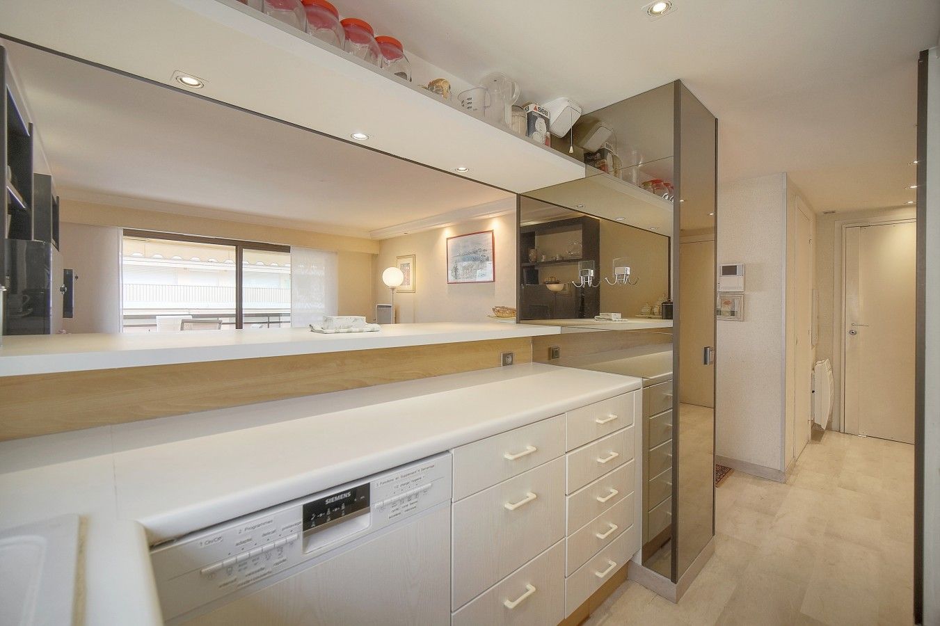 Une salle de bain moderne avec un grand miroir, des meubles blancs et un lave-vaisselle apparent.