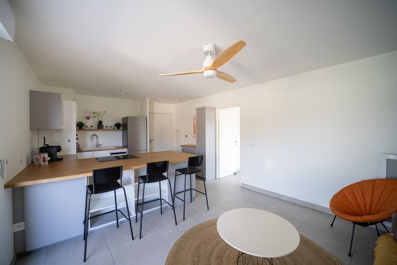 A modern kitchen with a central island, black bar stools, and a ceiling fan.