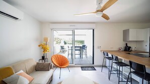 Uma sala moderna com sofá, mesa de jantar, cozinha e porta de vidro deslizante para um pátio externo.