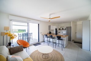 A modern kitchen with a central island, a dining area with chairs, and a sofa with a view to a patio. - One-bedroom apartment in Antibes, France (Antibes)