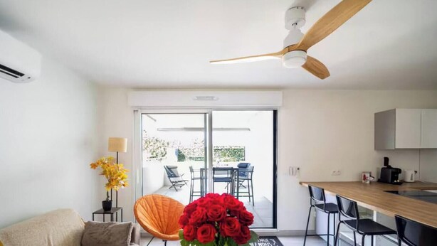 Uma sala moderna com sofá, área de jantar com mesa e cadeiras, cozinha com armários e ventilador de teto.