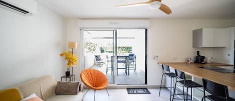 A modern living space with a sofa, a dining table, a chair, and a kitchen area with cabinets and a coffee machine.