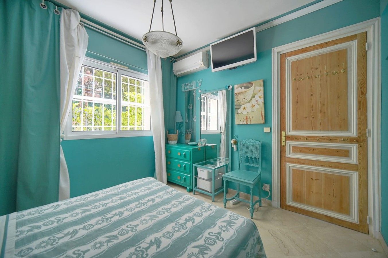 A bedroom with a bed, a dresser, a chair, a television, and a door.