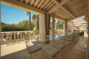 An outdoor patio with a glass-top table and chairs, surrounded by a balustrade and palm trees. - Nine-bedroom home in France, Antibes (Antibes)