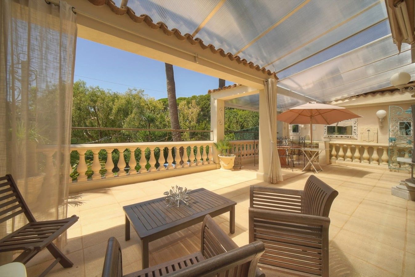Um pátio coberto ao ar livre com mesa e cadeiras, uma pérgola e vista para o verde.