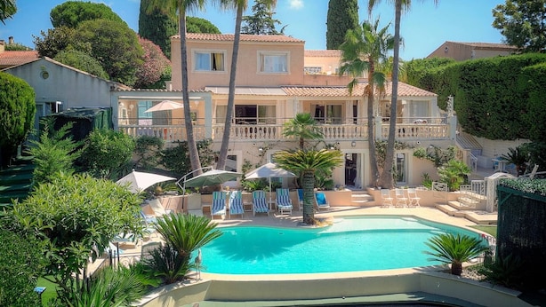 A pool area with lounge chairs, palm trees, and a building with balconies. - VILLA MÉVANIA antibes (Antibes)