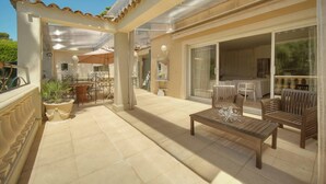 A covered patio with a wooden table and chairs, a potted plant, and a sliding glass door leading to an interior space. - VILLA MÉVANIA antibes (Antibes)
