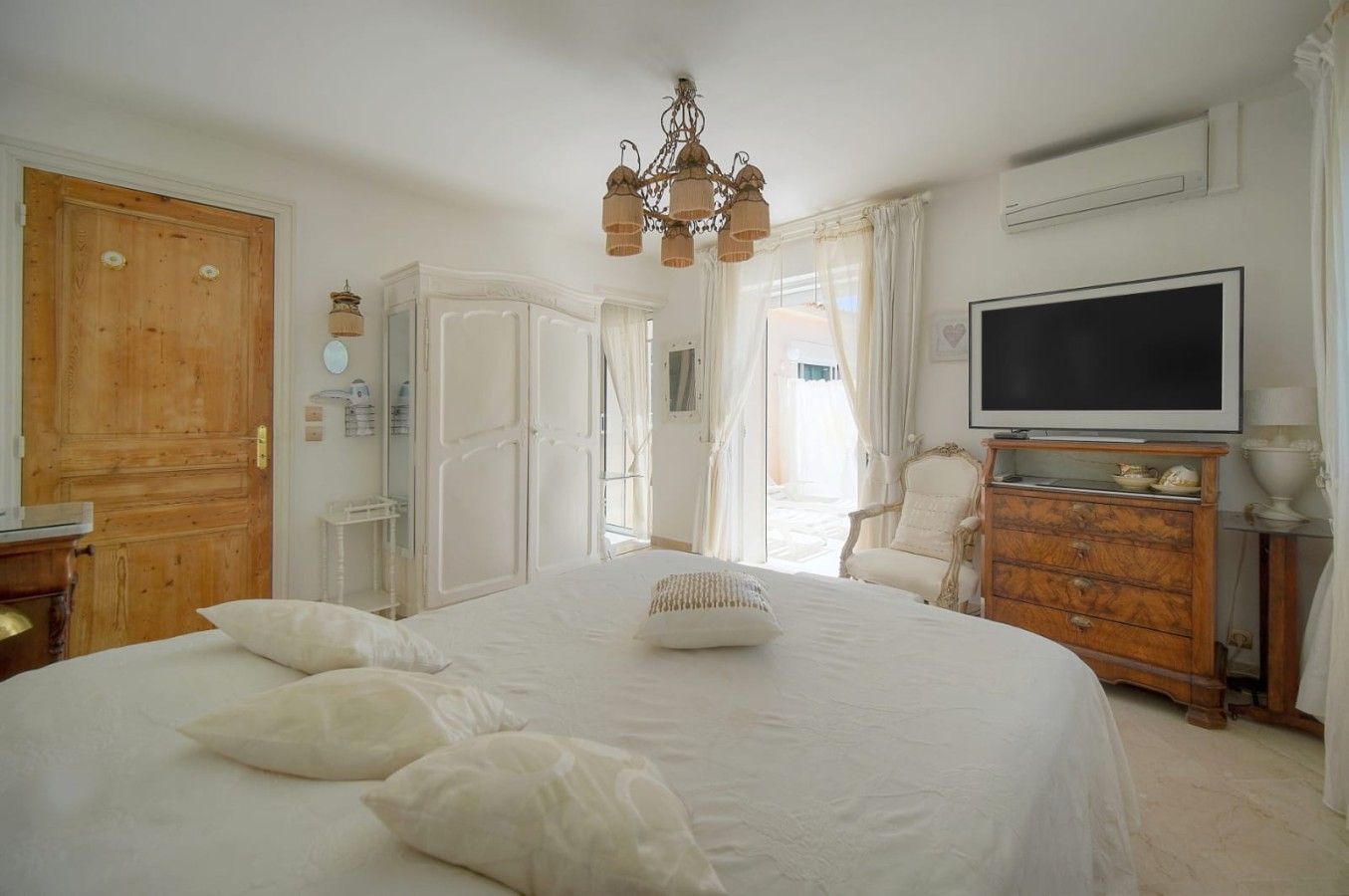 A bedroom with a large bed, a television, a wooden dresser, and a chandelier.