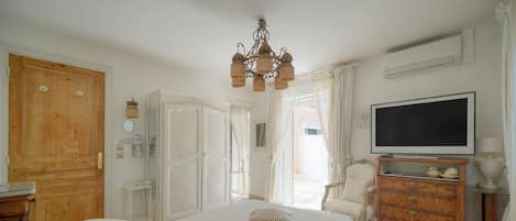 A bedroom with a large bed, a television, a wooden dresser, and a chandelier.