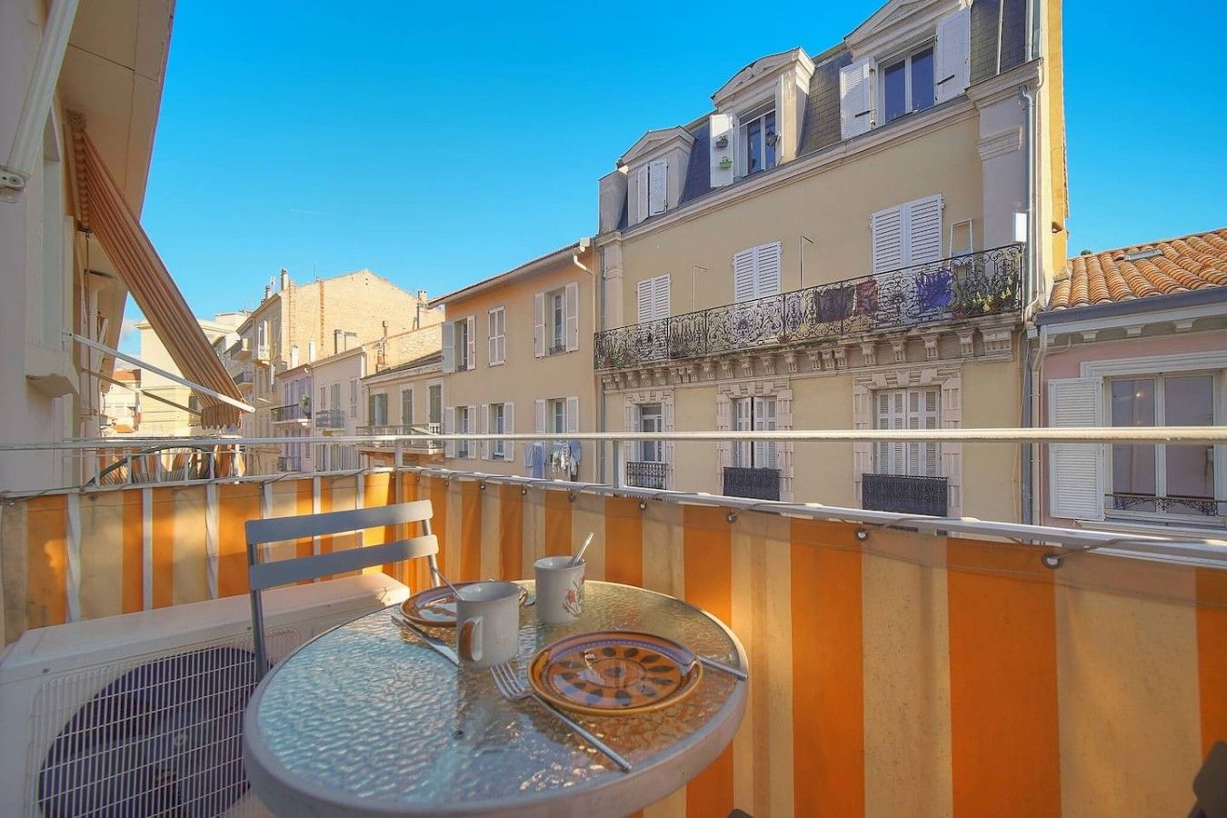 Un balcon avec une table dressée pour deux personnes, une chaise et un appareil de climatisation.