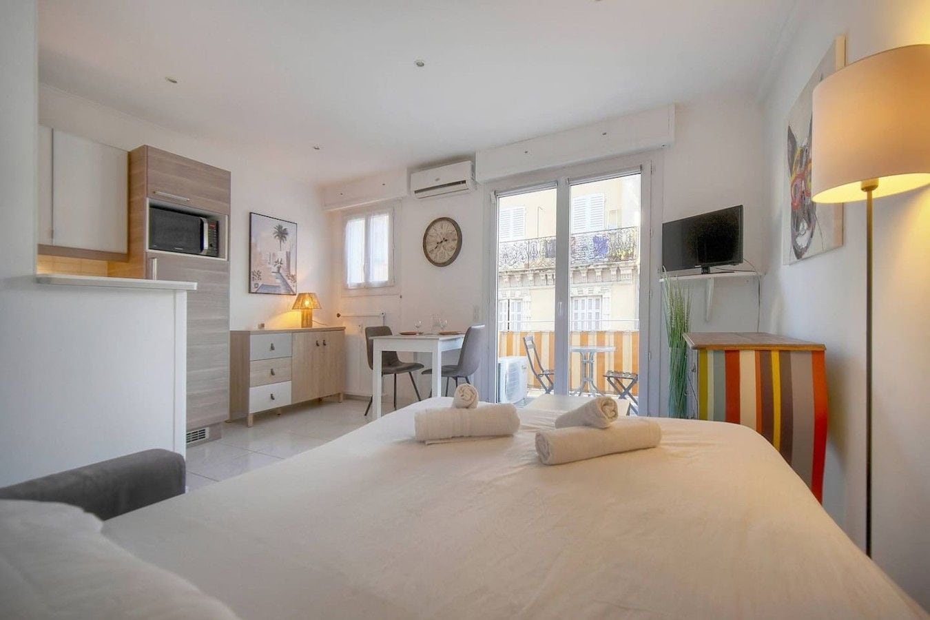 Habitación de hotel con cama, escritorio, silla, televisor y balcón con vistas.
