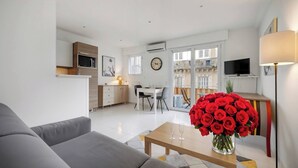 A modern living room with a sofa, a dining table with chairs, a kitchen area, and a TV. - LE CLEMENCEAU (Cannes)