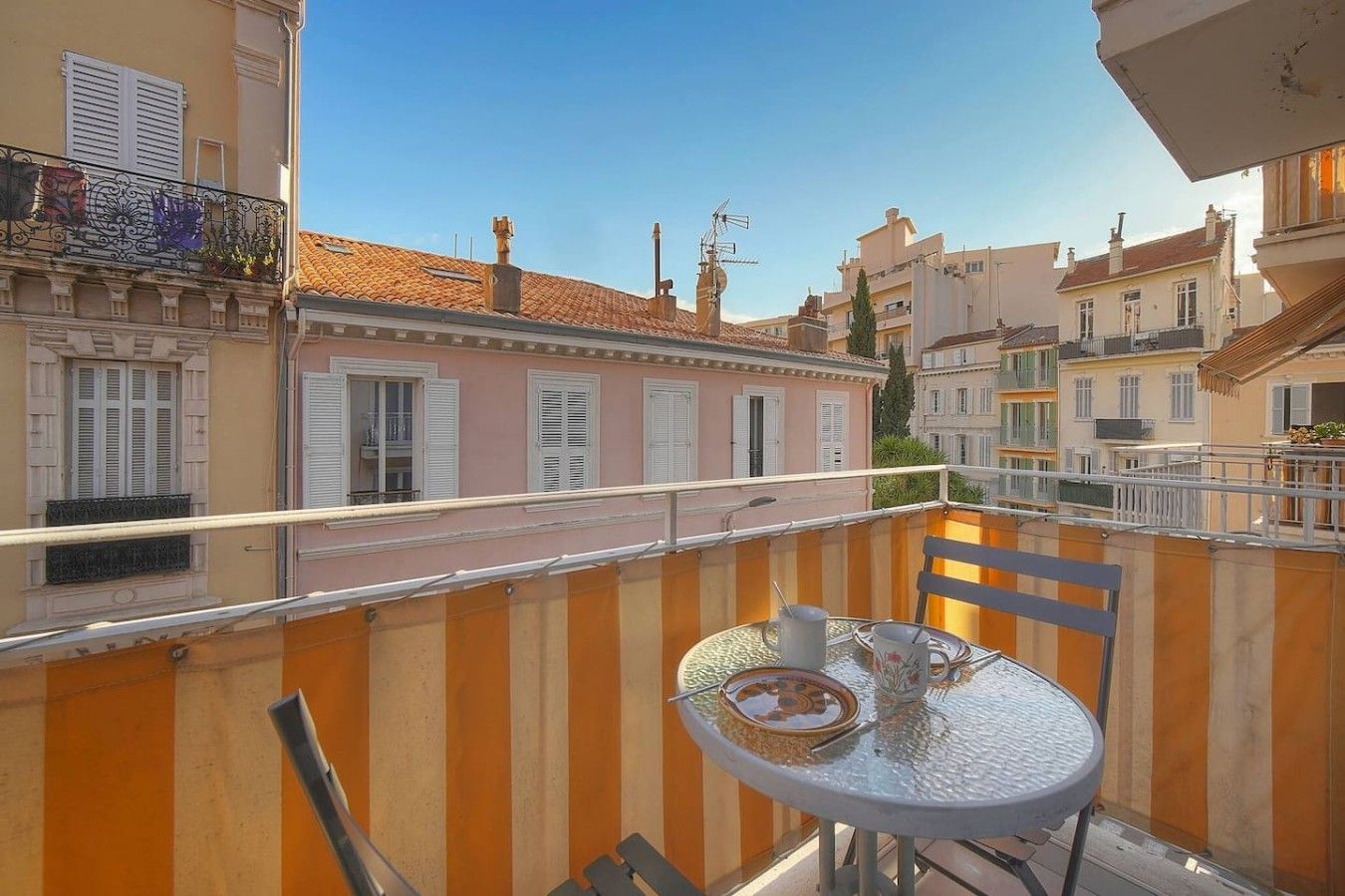 Un balcón con mesa y sillas, con vistas a una hilera de edificios de arquitectura tradicional.