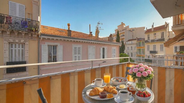 A balcony with a table set for breakfast, including croissants, fruit, and coffee. - LE CLEMENCEAU (Cannes)