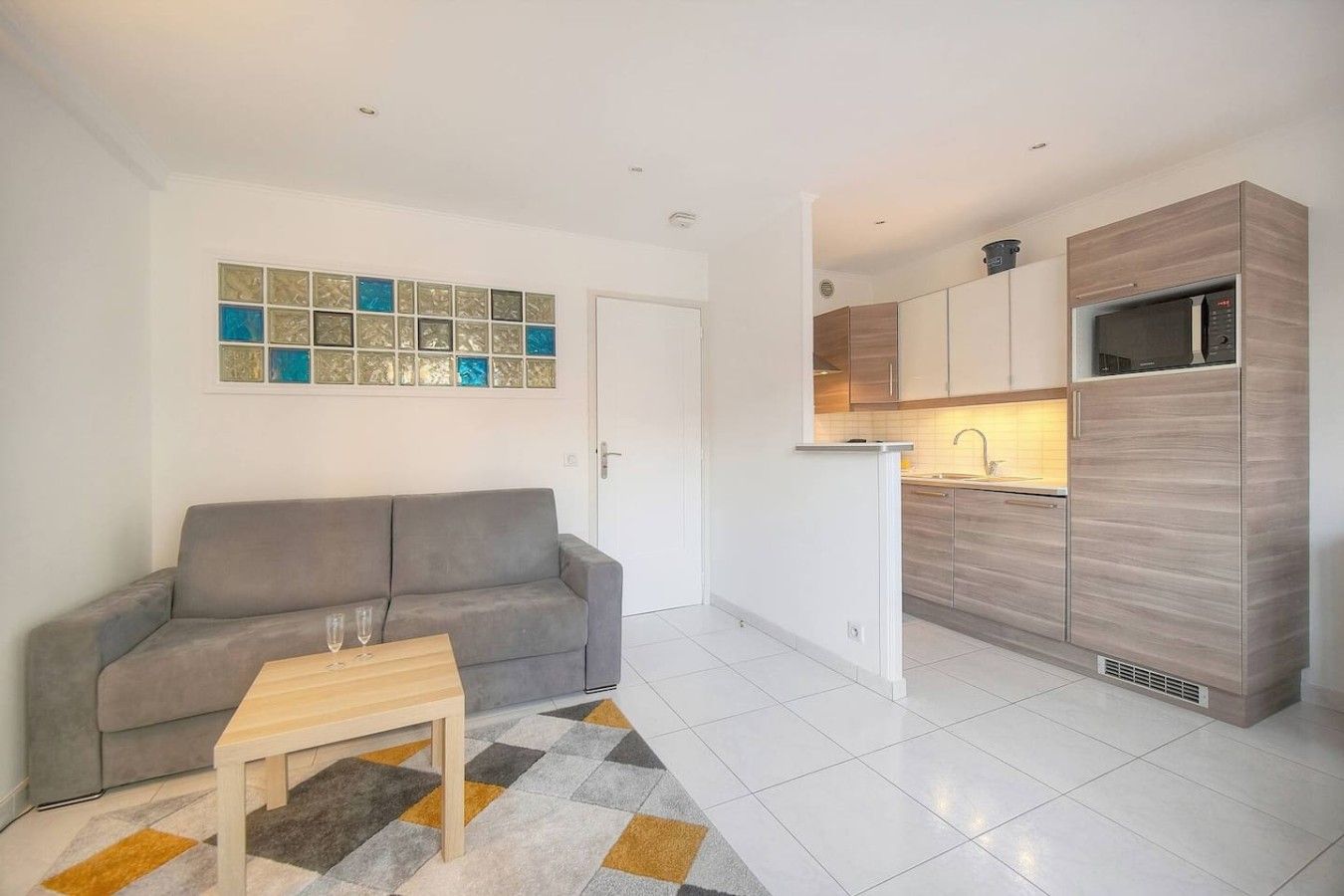 A compact living space with a sofa, a small table, a kitchen with modern appliances, and a decorative wall.