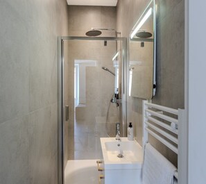 Un bagno moderno con doccia vetrata, lavandino bianco e porta asciugamani.