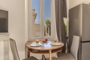 A dining area with a table set for two, a refrigerator, and a window with a view of buildings and greenery. - Three-bedroom apartment in France, Cannes (Cannes)