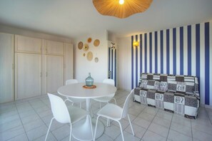Zona de menjador amb taula rodona, cadires blanques, un vas decoratiu i una paret amb ratlles.