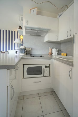 Una cuina compacta amb armaris blancs, microones, bullidor d'aigua i cafetera.