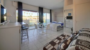 Une chambre d’hôtel équipée d’une kitchenette, d’un coin repas, d’un lit et d’un balcon offrant une vue sur les palmiers.